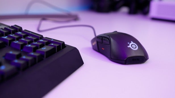 RivalSteelSeries Rival 700 gaming mouse next to keyboard with backlight.