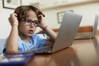 A boy wearing specs looking at a laptop kept on a table