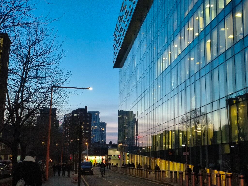 City street at dusk with modern buildings and pedestrians.