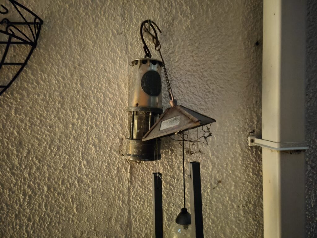 Decorative lamp and wind chimes on textured wall.