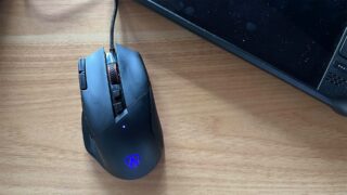 AOC Agon AGM600 gaming mouse on wooden desk beside laptop.