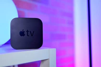 A black Apple TV device on a white shelf with purple lighting.