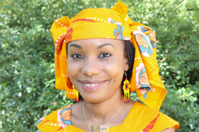 A Chadian woman in yellow headdress smiles against leafy background