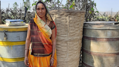 Tribal woman in yellow and brown dress and headscarf stands next to a silo in India