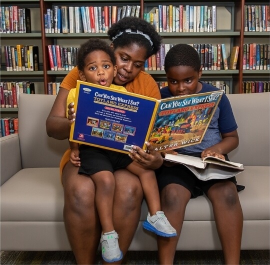 Family Of Three Reading A Children’s Book Together At Kaltreider Benfer Library