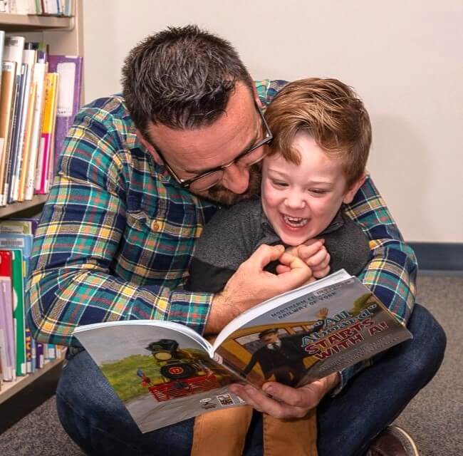 Father And Son Giggling Reading Together