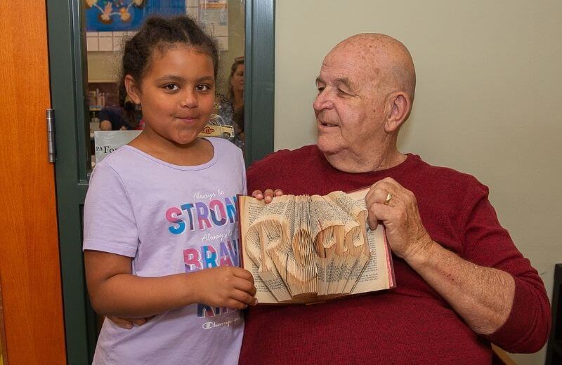 granddaughter and grandfather smiling at each other while he holds an open book that says the word "read" on it