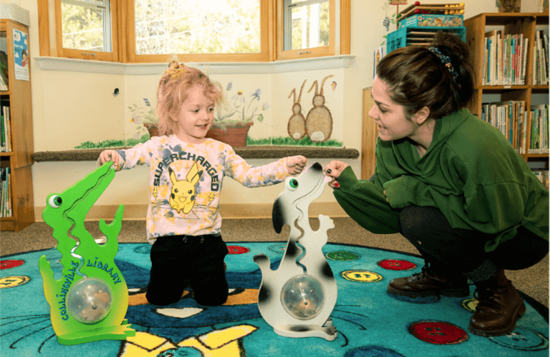 A little child feeds coins to two "belly banks" as their smiling mother looks on